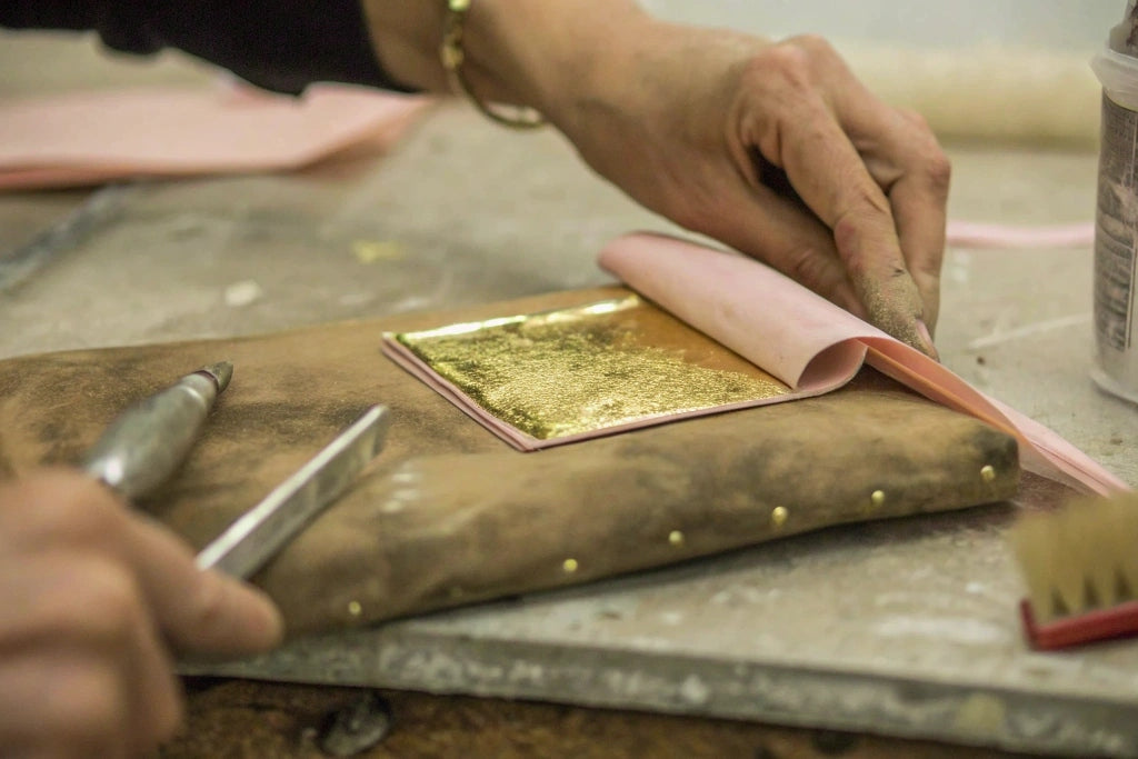 A woman carefully working with gold leaf in an artisanal workshop.